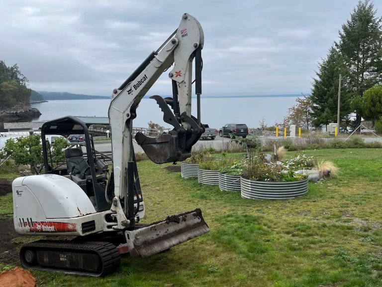 A Bobcat mini-excavator on a lawn by the water